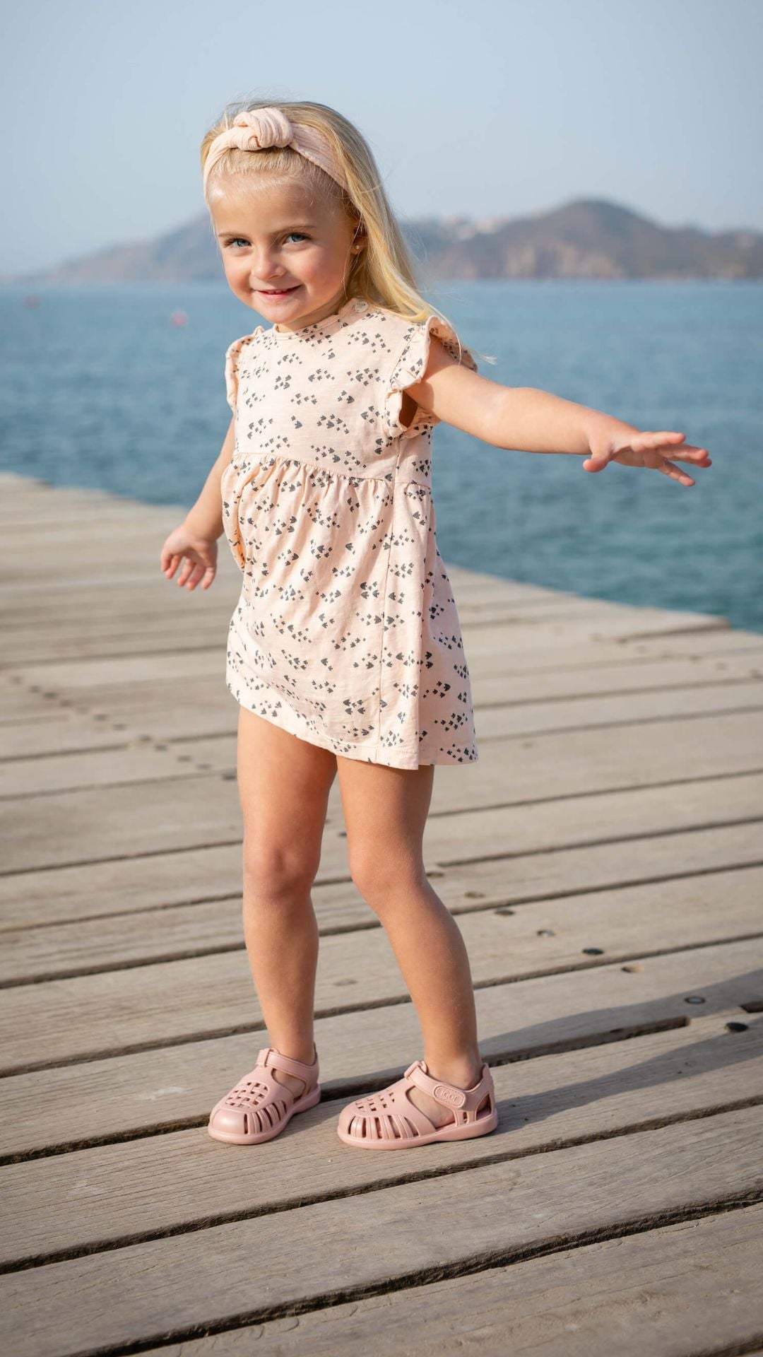 petite fille blonde sur un pont en bois avec des sandales de plage rose