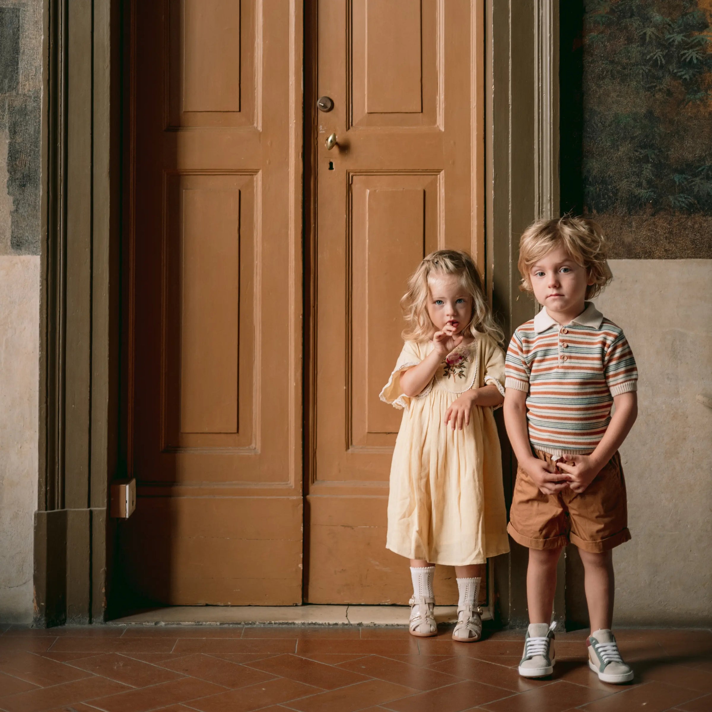 bébé fille et petit garçon en chaussures babybotte devant une grande porte